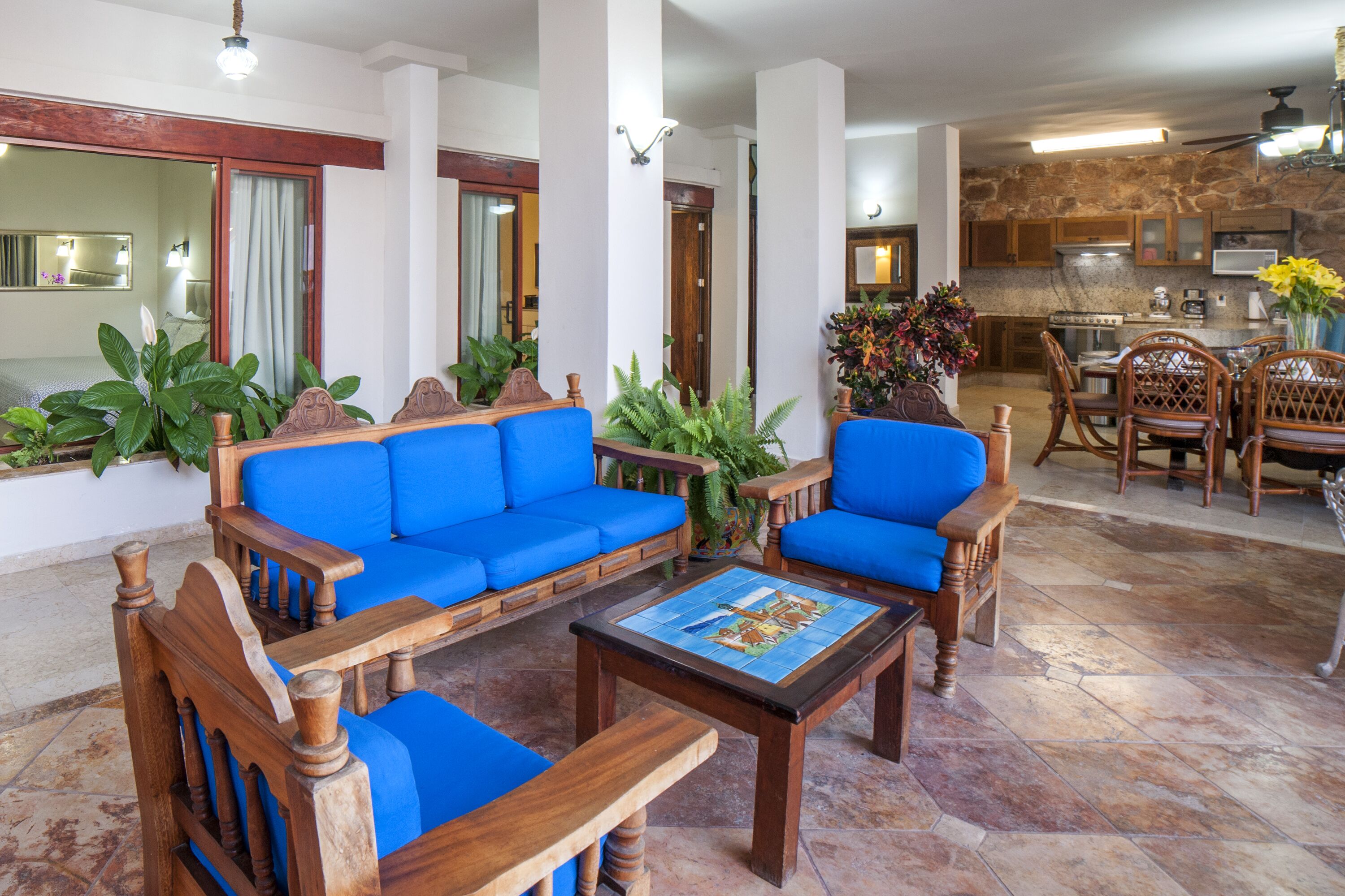 Ein geräumiger Wohnbereich mit blauem Sofa, Holzstühlen, einem Couchtisch und einer Küche im Hintergrund.