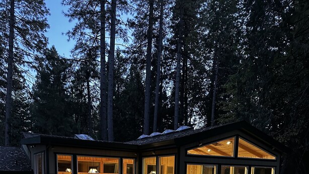 Eine moderne, gläserne Hütte mit einem Kiesweg, der zum Eingang führt, umgeben von dichtem Wald.
