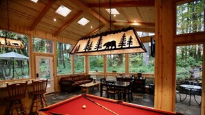 Ein gemütlicher Innenpoolbereich mit Billardtisch, Sitzgelegenheiten und großen Fenstern mit Blick auf den umliegenden Wald.