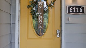 A yellow front door with a 'WELCOME' sign, a mailbox, and a house number '6116'. - Cozy and Conveniently located close to KCI (KCMO)