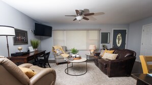 A living room with a ceiling fan, a TV mounted on the wall, a sofa, a coffee table, and a chair. - Cozy and Conveniently located close to KCI (KCMO)