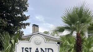 Une enseigne indiquant « Island Square Condominium », entourée d’une végétation luxuriante et de plantes en fleurs.