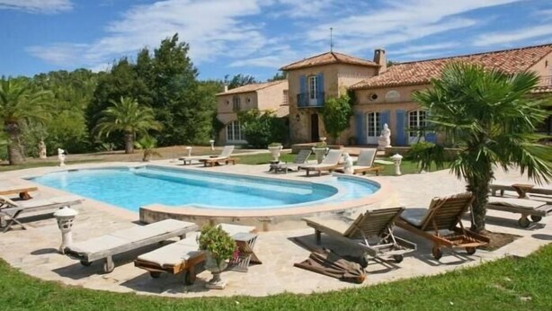 A pool area with lounge chairs and a house in the background.