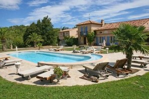 Zona de piscina con sillones de descanso y una casa al fondo.