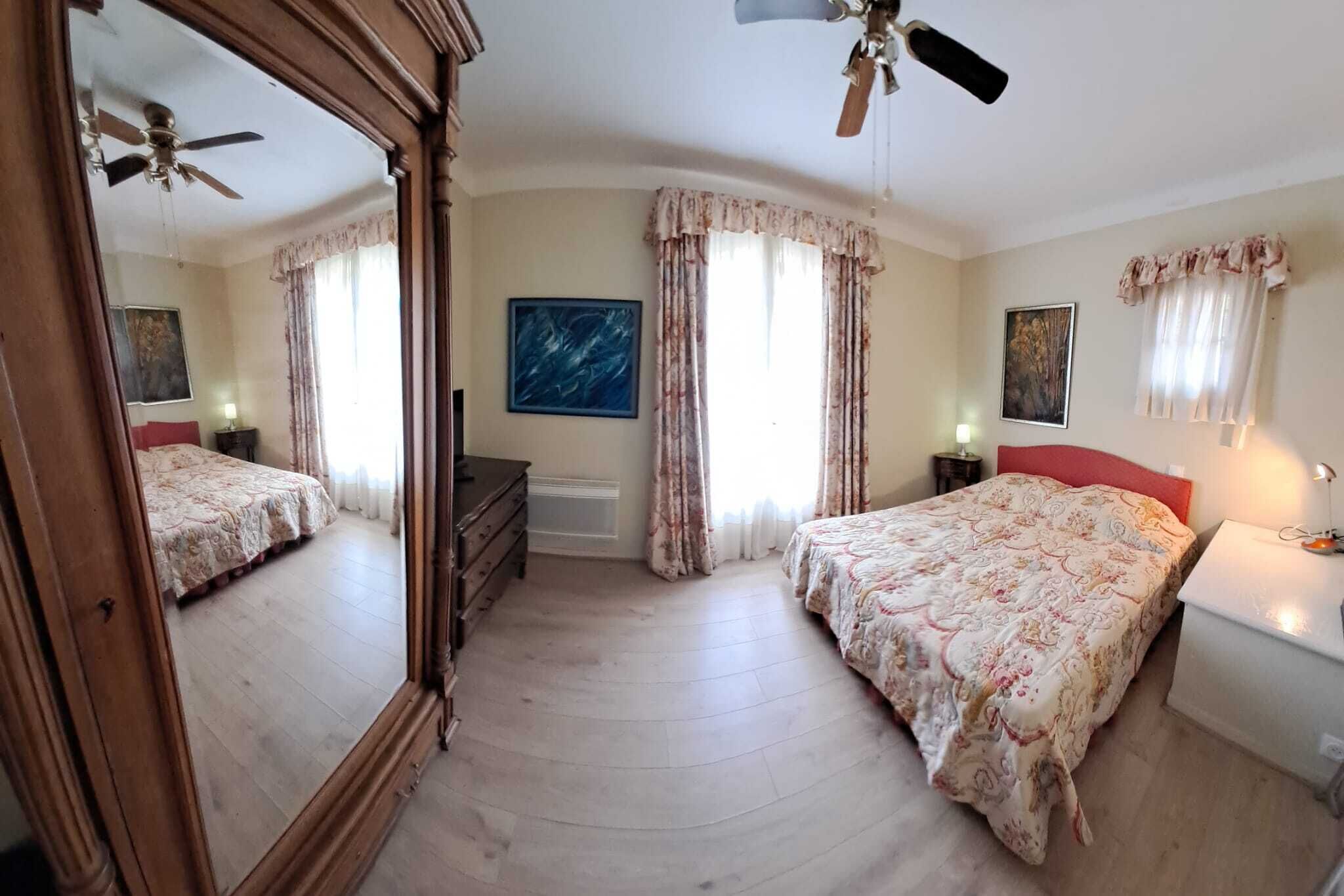 A bedroom with two beds, a ceiling fan, a large mirror, and a nightstand with a lamp.
