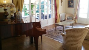 A room with a grand piano, a sofa, and a chair, with a large window and curtains.