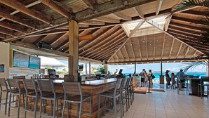 Angolo bar all'aperto con travi in legno, pavimento piastrellato e vista sulla spiaggia.