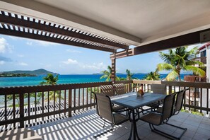 A balcony with a table and chairs, overlooking a coastal view with palm trees and a clear sky. - Luxurious, Penthouse, 2 level, corner unit Oceanfront condo at Sapphire Beach (St Thomas)