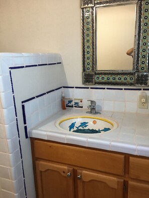 A bathroom with a white sink, blue and white tiles, a wooden cabinet, and a decorative mirror with a floral pattern.