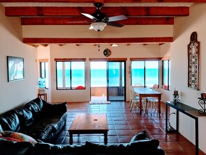A spacious living area with a ceiling fan, a wooden coffee table, a leather sofa, and a view of the ocean through large windows. - PROMO-Beach Front on a Sandy Beach, Hi speed Wi-Fi- Gated community (San Felipe)