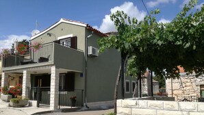 Un edificio de dos pisos con balcón, pared de piedra y un árbol en frente.