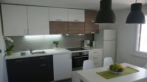 Una cocina moderna con armarios blancos y de madera oscura, un lavamanos de acero inoxidable, un horno empotrado y un comedor con una mesa dispuesta para dos.