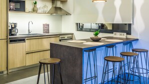 Een moderne keuken met houten kastjes, een inbouwoven, een koffiezetapparaat en een bar met krukjes.