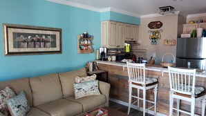 Un salon chaleureux avec un canapé et des fauteuils, une cuisine dotée de meubles en bois et un coin repas avec un bar.