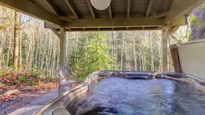 Ein Whirlpool in einem überdachten Außenbereich mit einem Stuhl und Blick auf einen Wald.