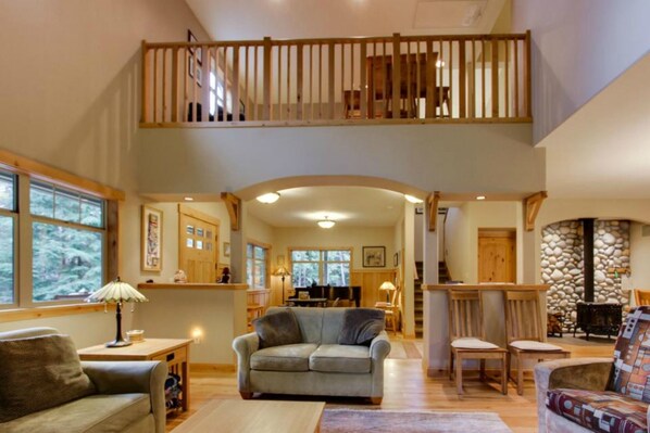A spacious living area with a high ceiling, a wooden staircase, and a stone fireplace.
