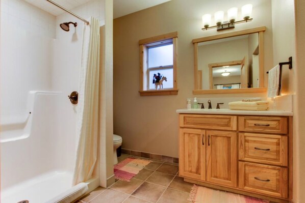 A bathroom with a bathtub, a toilet, a vanity with a mirror, and a window with a view of a horse.