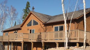A two-story wooden cabin with a balcony, large windows, and a chimney.