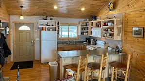 A wooden interior with a kitchen area featuring a central island, wooden chairs, and a ceiling fan.