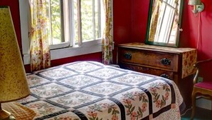 Una habitación con cama, cómoda, espejo y ventana con cortinas.