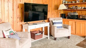 Una sala de estar con televisión, dos sillones, una mesita y una estantería.
