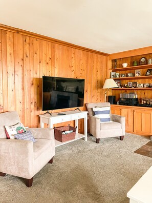 Una sala de estar con televisión, dos sillones, una mesita y una estantería.