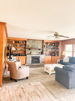 A cozy living room with a fireplace, wooden bookshelves, a ceiling fan, and comfortable seating.