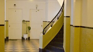 Un couloir avec un sol à carreaux, un escalier doté d’une rampe noire et deux portes blanches portant des numéros.