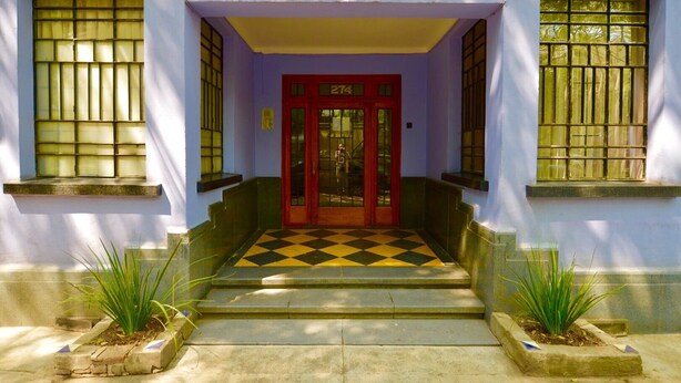 L’entrée d’un immeuble avec une porte rouge, le numéro 274, et un motif de carreaux sur le sol.