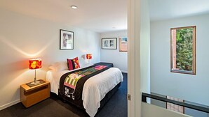 A hotel room with a bed, a nightstand with a lamp, framed pictures on the wall, and a window with a view of greenery. - Fitzgeorge - spacious home in inner Fitzroy Melbourne perfect location (Fitzroy)