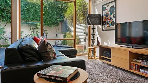 A modern living room with a black leather sofa, a television, and a bookshelf. - Fitzgeorge - spacious home in inner Fitzroy Melbourne perfect location (Fitzroy)