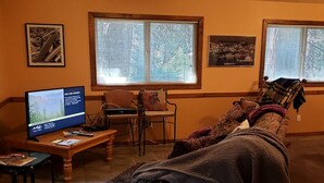 Een woonkamer met een bank, een televisie en een raam met zonwering.
