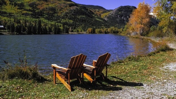 Two wooden Adirondack chairs facing a lake with a forested hillside in the background. - ADORABLE  CABIN WITH AMAZING MOUNTAIN VIEWS CLOSE TO GORE MT (North River)
