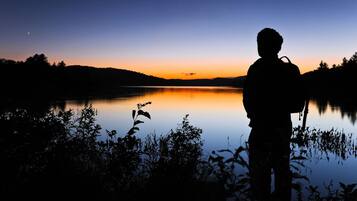 A silhouette of a person standing by a calm lake at sunset.