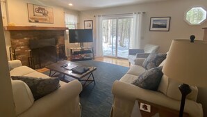 A living room with a fireplace, a television, and a large window with a view of trees.