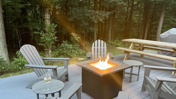 A deck with Adirondack chairs, a square fire pit, and a picnic table.