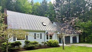 A two-story house with a metal roof, a garage, and a well-maintained lawn.