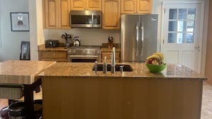 A kitchen with wooden cabinets, stainless steel appliances, granite countertops, and a green bowl of fruit.