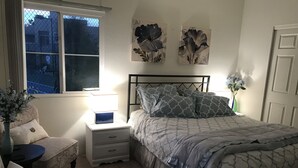 Ein Schlafzimmer mit Bett, Nachttischen, einem Sessel, einem Fenster und Wandbildern.