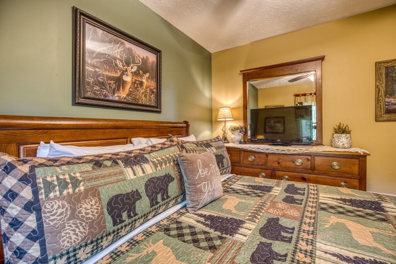 A bedroom with a large bed, a wooden dresser, a television, and a framed picture on the wall.