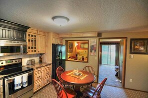 A compact kitchen with wooden cabinets, a microwave, an oven, and a dining area with a table and chairs. - Very nice Condominium in an excellent location! (West Yellowstone)