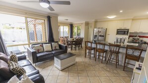 A spacious living area with a sofa, coffee table, and dining table. A kitchen with white cabinets and appliances is visible. - Home Away From Home! Large executive home with pool. (Mansfield)