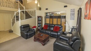 A spacious living room with a staircase, leather furniture, a piano, and a bookshelf. - Home Away From Home! Large executive home with pool. (Mansfield)
