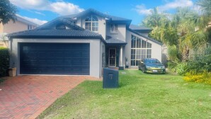 A two-story house with a black garage door, a driveway, and a green car parked in the driveway. - Home Away From Home! Large executive home with pool. (Mansfield)