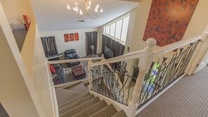 A staircase leading to a living area with a chandelier, a large window, and a red floral wall art piece. - Home Away From Home! Large executive home with pool. (Mansfield)