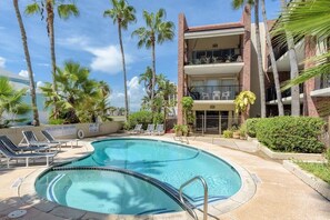 A pool area with lounge chairs, palm trees, and a two-story building with balconies. - Unit 101 Villa Del Sol (South Padre Island)