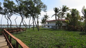 A wooden deck leading to a grassy area with a view of a body of water and a building with a red roof.
