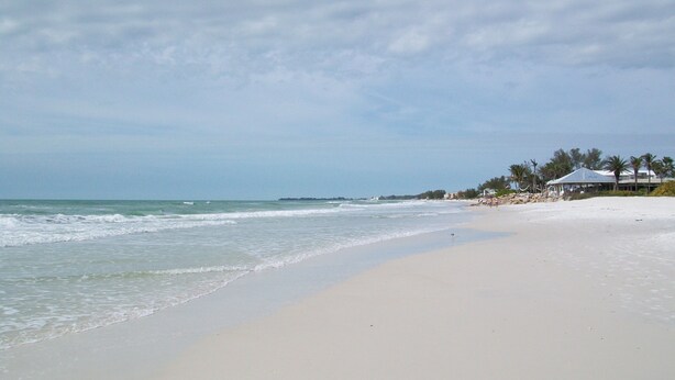 A beach with a sandy shore, a few buildings, and a clear sky.