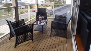 Un balcon agrémenté de meubles en osier, une table avec une bouteille et un verre, et une vue sur un quartier résidentiel.