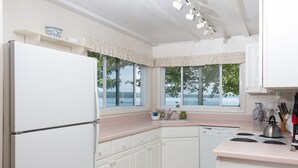 Cocina con gabinetes blancos, un refrigerador, un fregadero y una estufa. Hay ventanas con vista a árboles y una masa de agua.